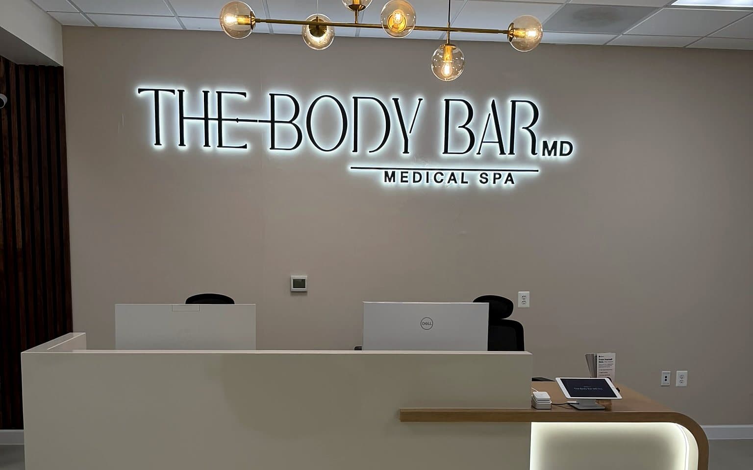 The reception at The Body Bar MD with its sculpted ceiling, gold chandelier and illuminated logo