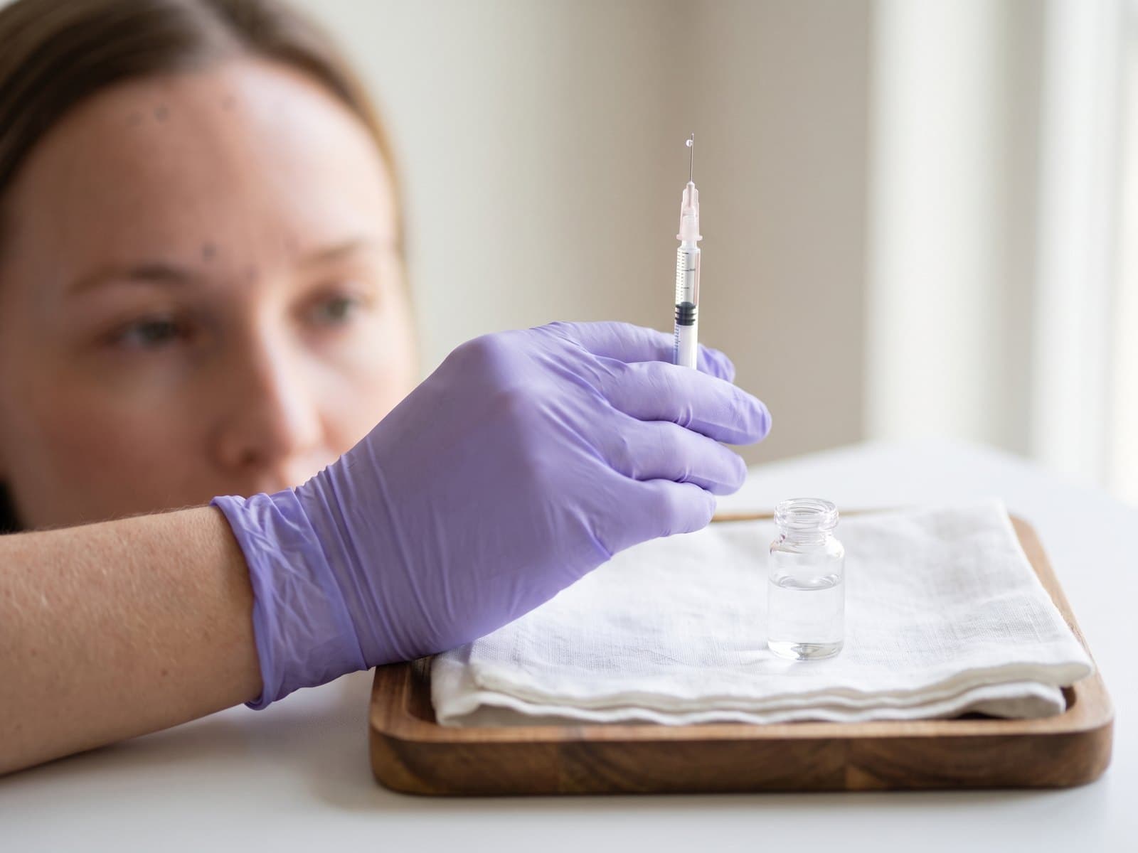 A gloved hand holding a fine-gauge syringe beside a small glass vial