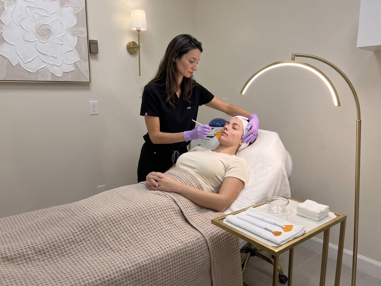 A nurse painting chemical peel solution onto a woman's cheek with a soft fan brush